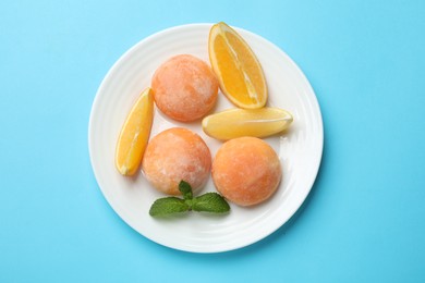 Photo of Plate with tasty mochi, cut orange and mint on light blue table, top view