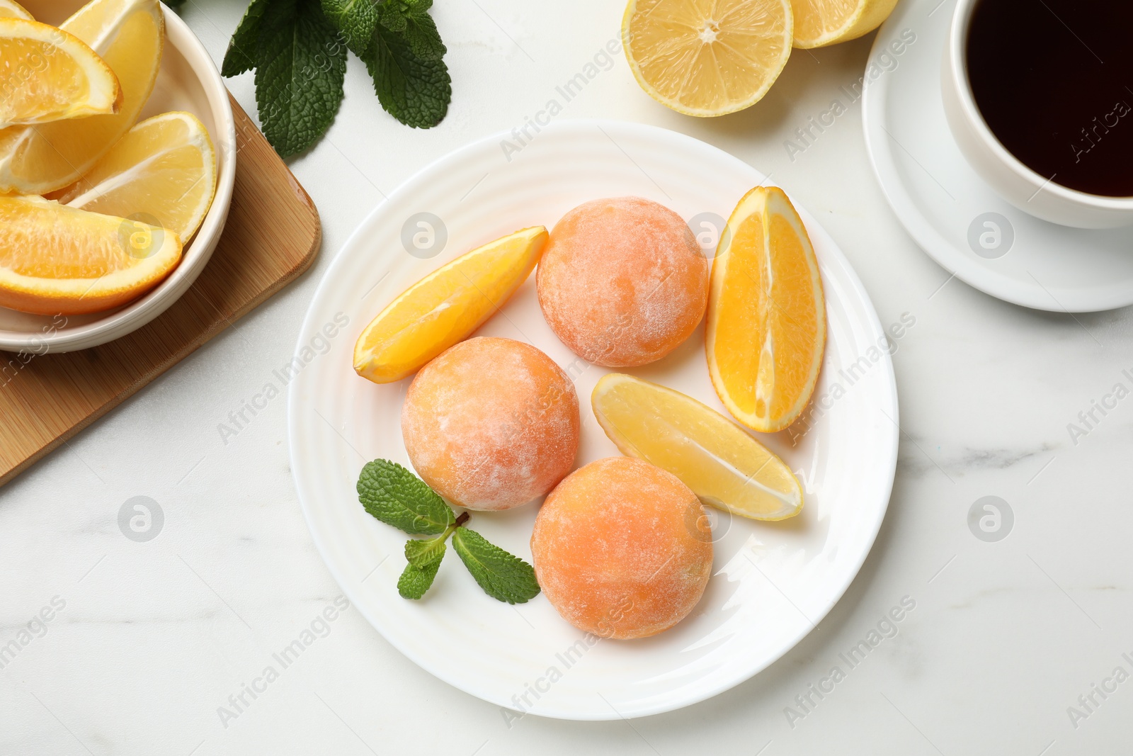 Photo of Plate with tasty mochi, cut orange, lemon and mint on white marble table, flat lay