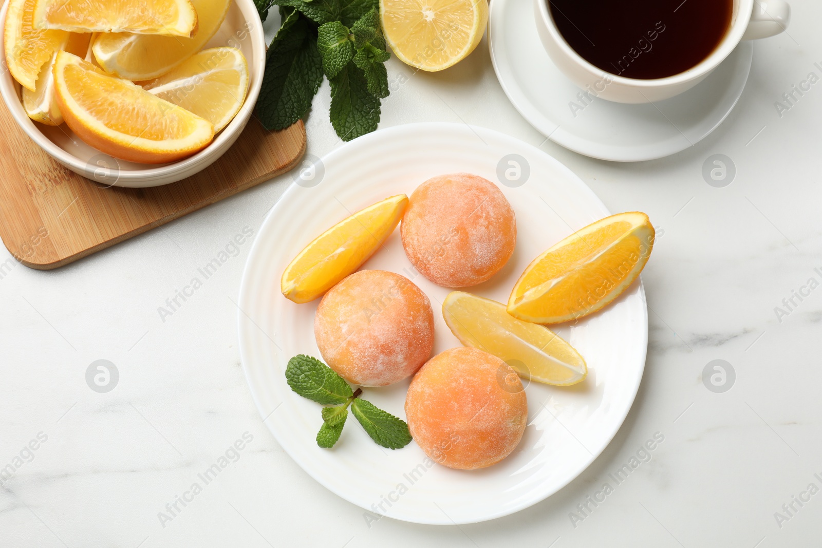 Photo of Plate with tasty mochi, cut orange, lemon and mint on white marble table, flat lay