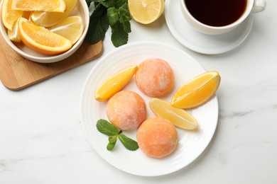 Photo of Plate with tasty mochi, cut orange, lemon and mint on white marble table, flat lay