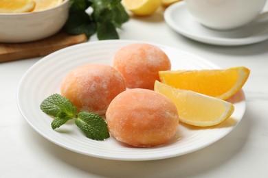 Photo of Plate with tasty mochi, cut orange, lemon and mint on white table, closeup