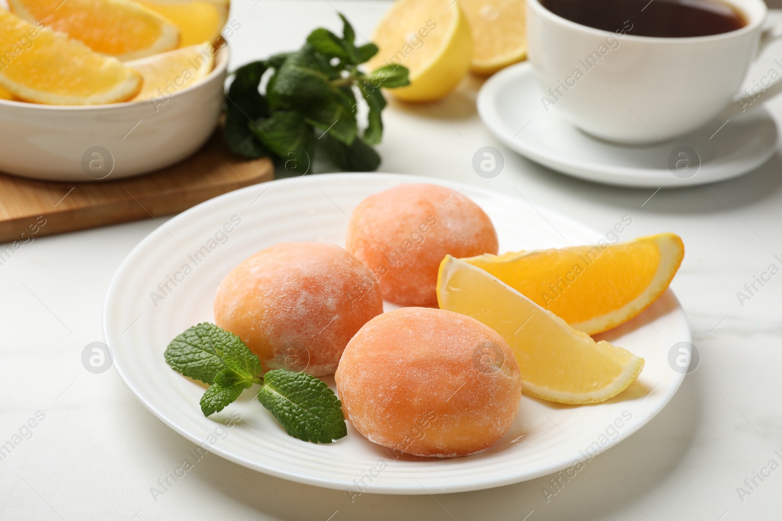 Photo of Plate with tasty mochi, cut orange, lemon and mint on white table, closeup