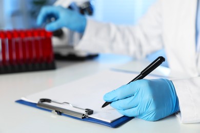 Photo of Laboratory testing. Doctor taking test tube with blood sample while working at table indoors, closeup