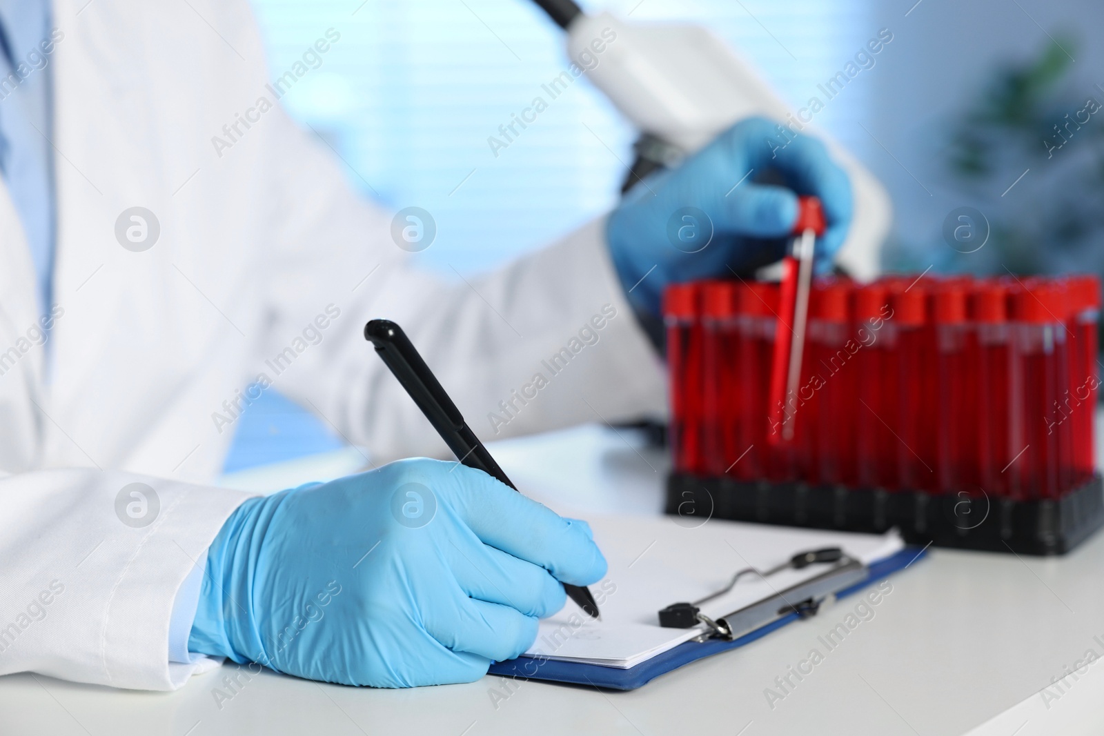 Photo of Laboratory testing. Doctor taking test tube with blood sample while working at table indoors, closeup