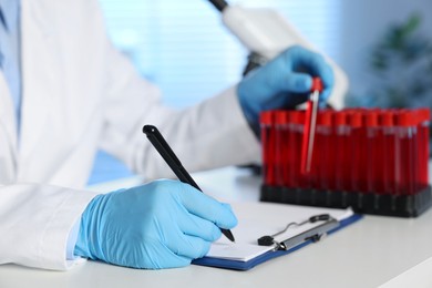 Photo of Laboratory testing. Doctor taking test tube with blood sample while working at table indoors, closeup