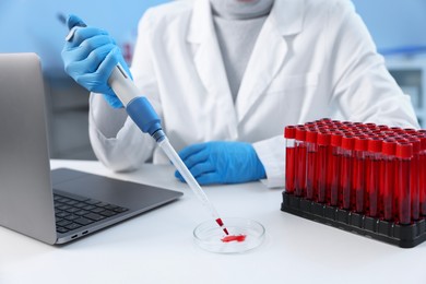 Photo of Laboratory testing. Doctor dripping blood sample into Petri dish at table indoors, closeup