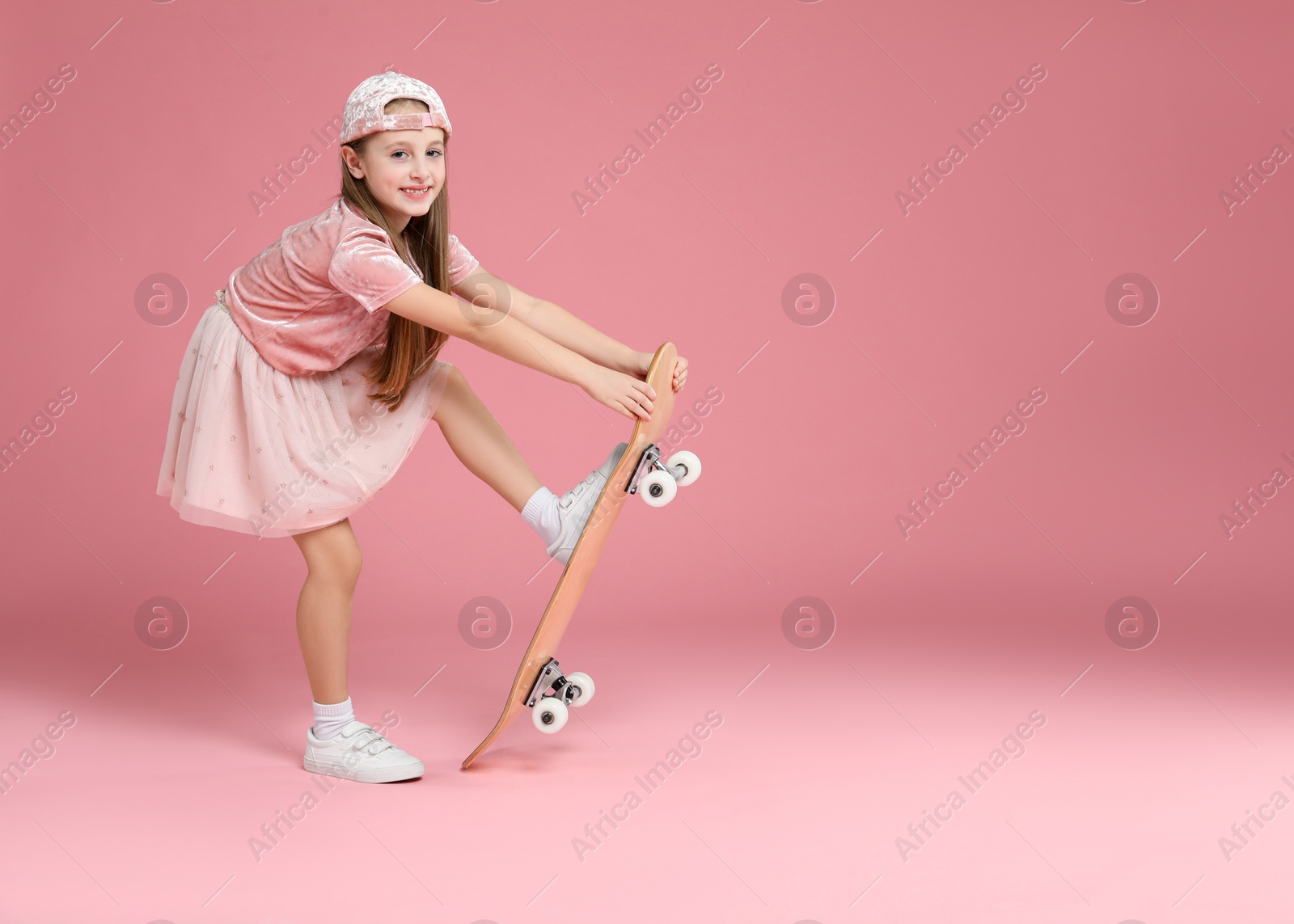 Photo of Little girl with skateboard against pink background, space for text