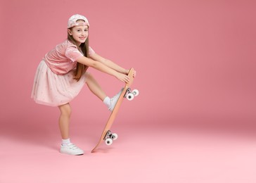 Photo of Little girl with skateboard against pink background, space for text