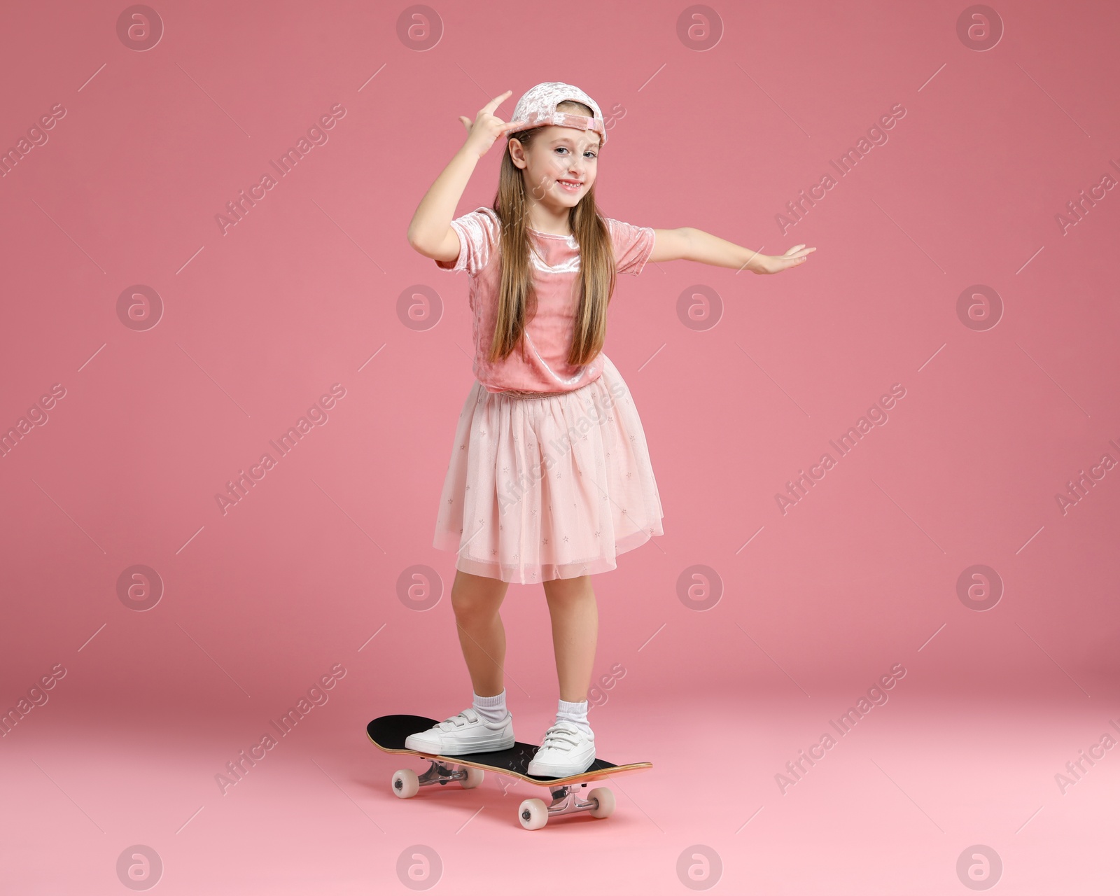 Photo of Little girl standing on skateboard against pink background. Space for text