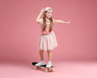 Little girl standing on skateboard against pink background. Space for text