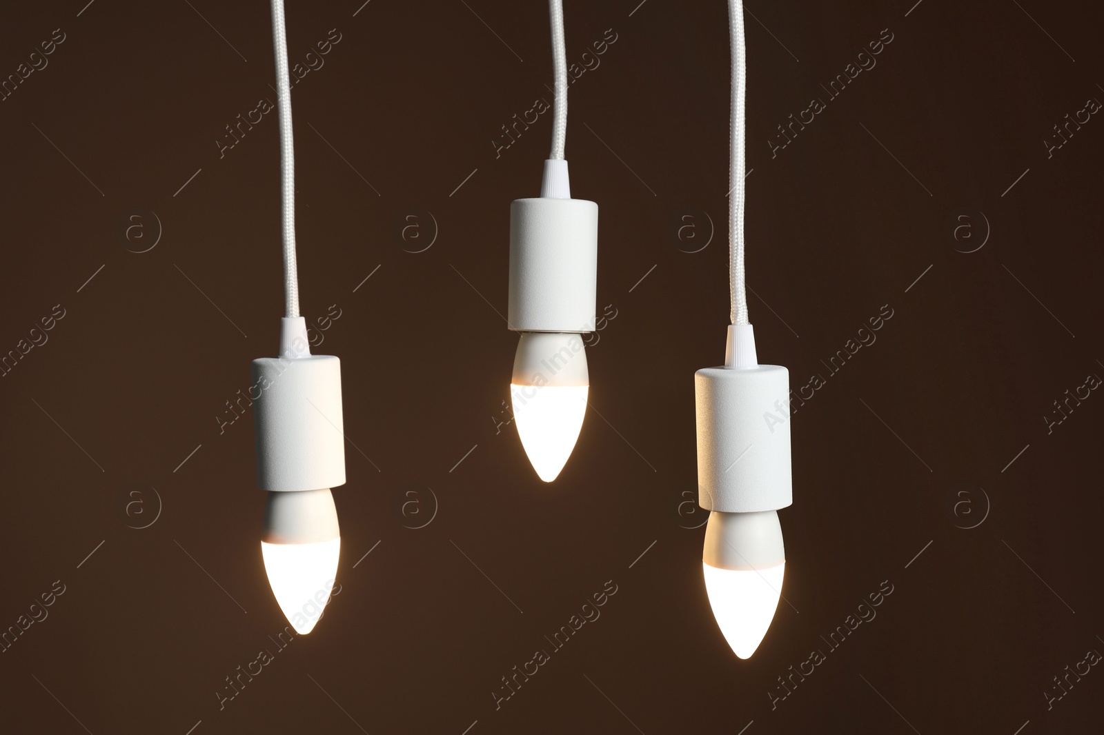 Photo of Light bulbs hanging on cords against brown background