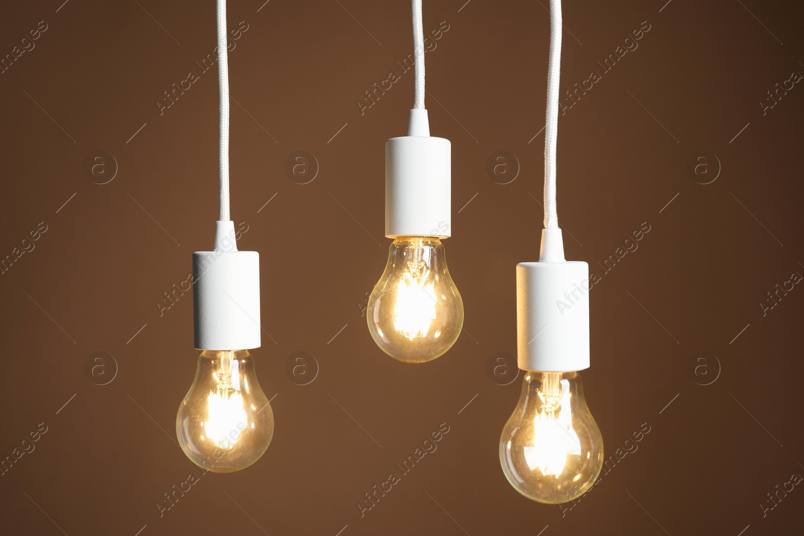 Photo of Light bulbs hanging on cords against brown background