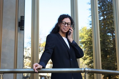 Portrait of young woman in stylish suit talking on phone outdoors