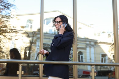 Portrait of young woman in stylish suit talking on phone outdoors