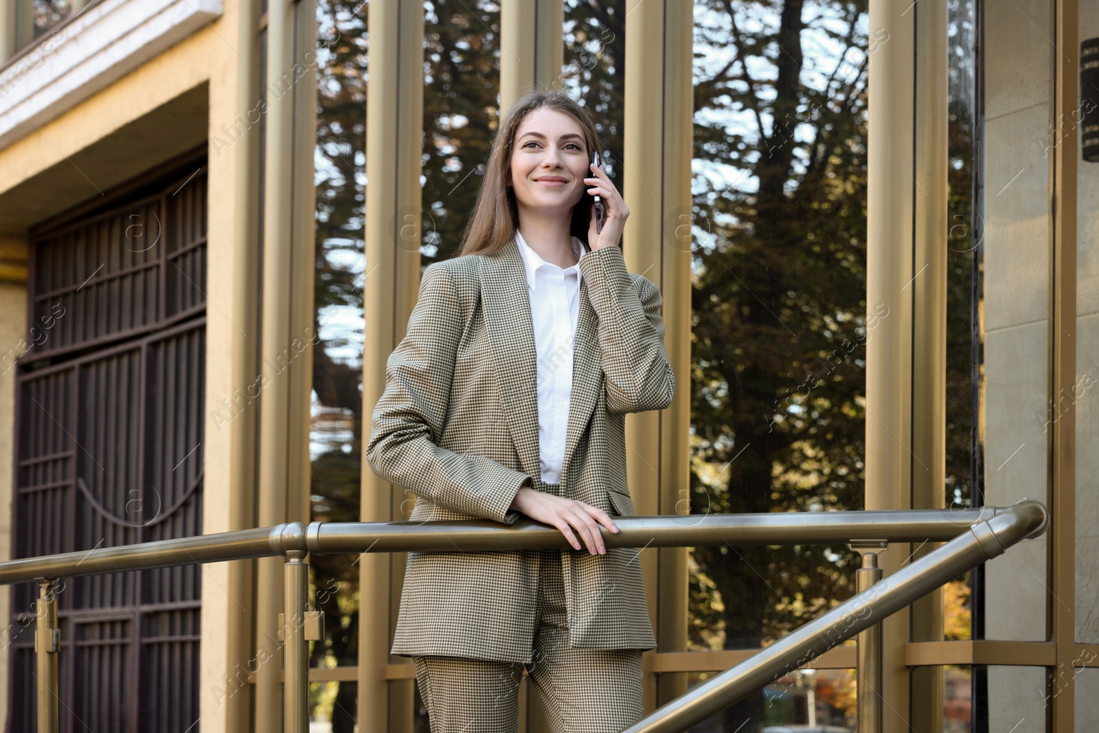 Photo of Portrait of young woman in stylish suit talking on phone outdoors