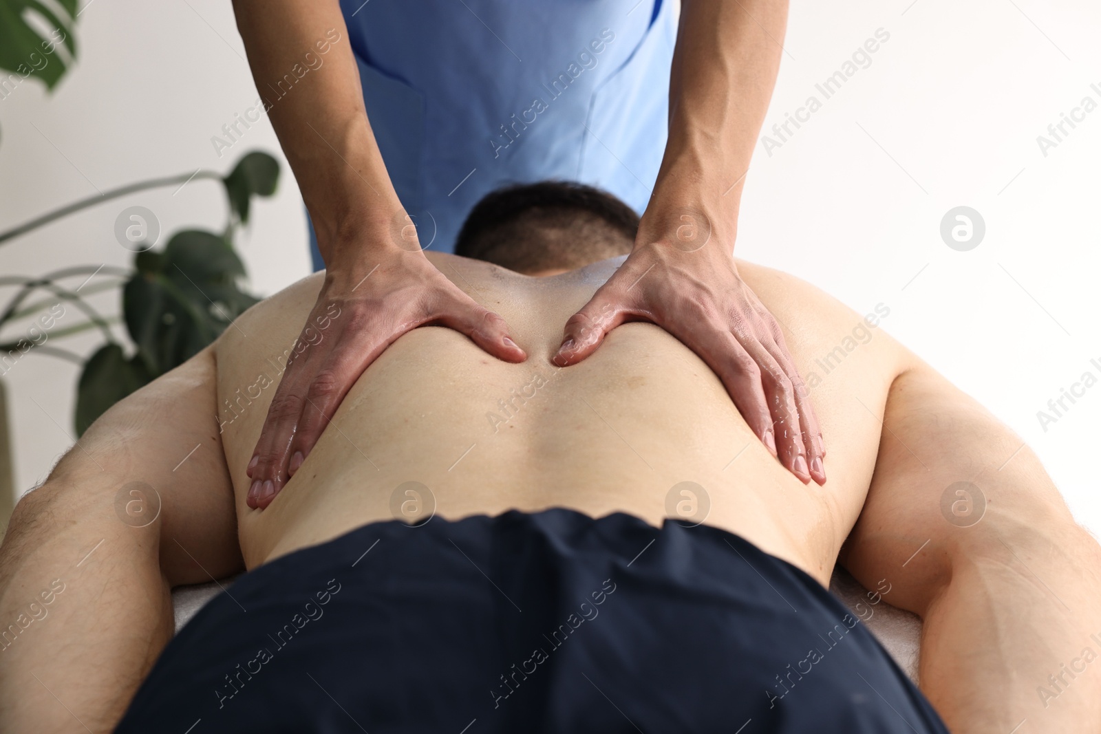 Photo of Professional physiotherapist doing back massage for his client indoors, closeup