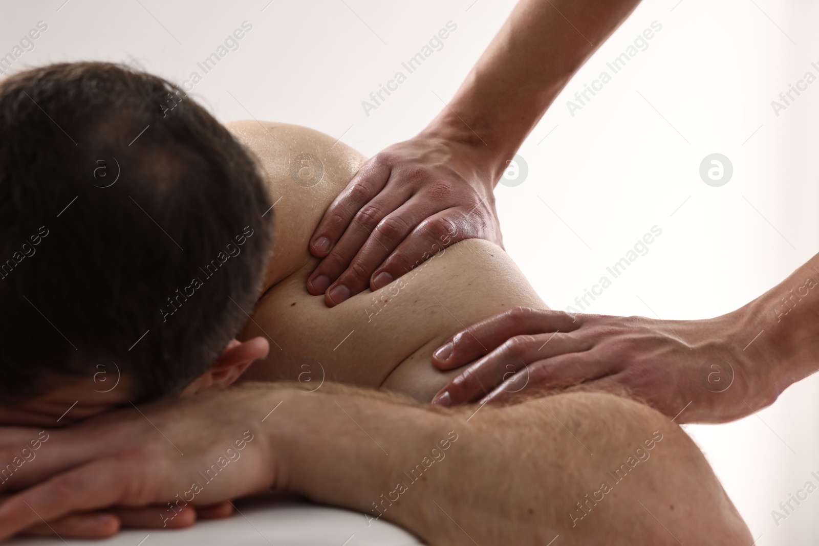 Photo of Professional physiotherapist doing shoulder massage for his client indoors, closeup