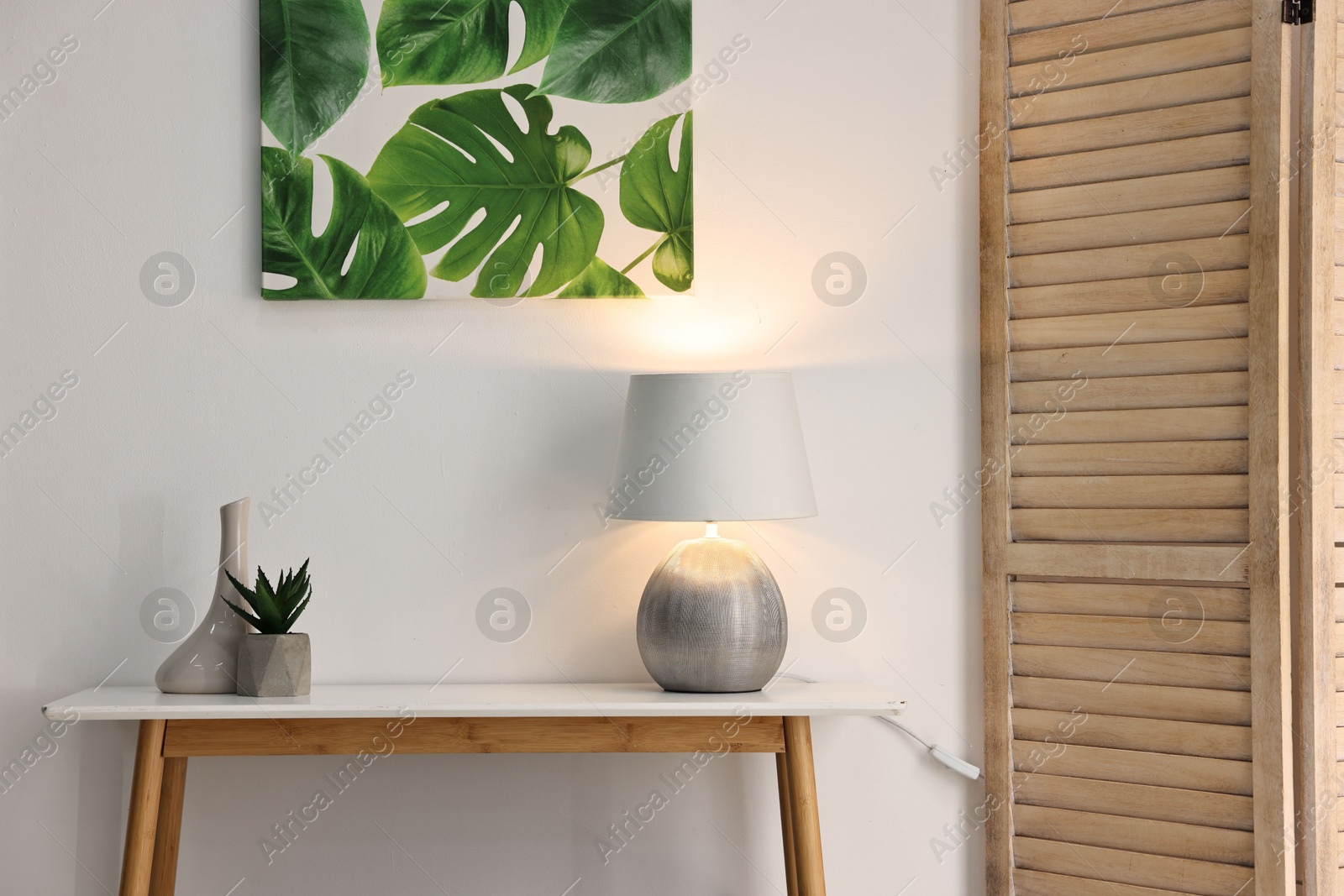 Photo of Stylish console table with lamp and decor near white wall indoors