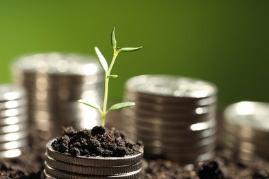 Money growth concept. Coins with young sprout in soil on green background, closeup. Space for text