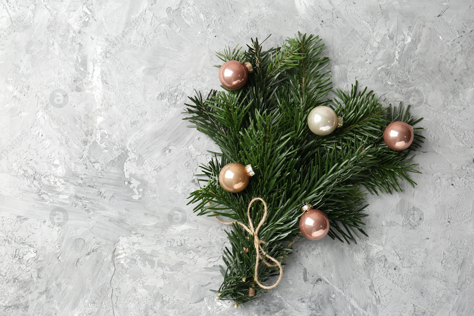 Photo of Festive bouquet of green fir branches with Christmas balls on grey textured background, top view. Space for text