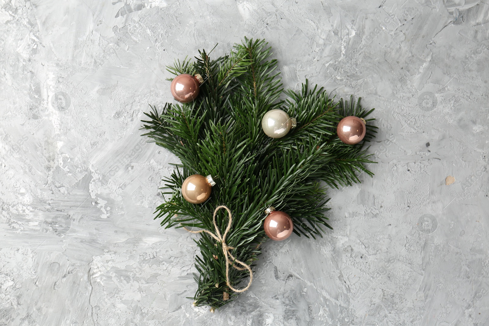 Photo of Festive bouquet of green fir branches with Christmas balls on grey textured background, top view