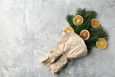 Photo of Christmas bouquet of fir branches with dry orange pieces wrapped in kraft paper on grey textured background, top view. Space for text