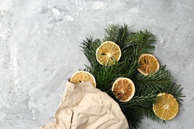 Photo of Christmas bouquet of fir branches with dry orange pieces wrapped in kraft paper on grey textured background, top view