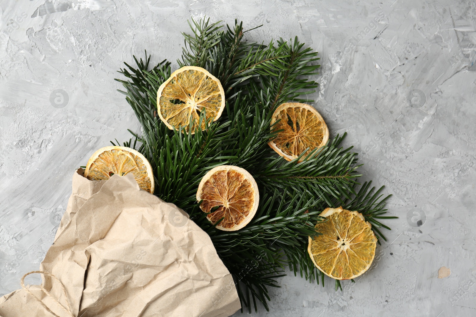 Photo of Christmas bouquet of fir branches with dry orange pieces wrapped in kraft paper on grey textured background, top view