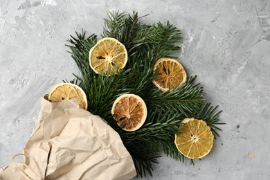 Christmas bouquet of fir branches with dry orange pieces wrapped in kraft paper on grey textured background, top view