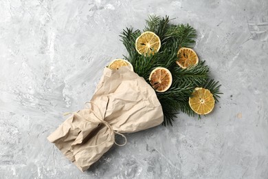 Photo of Christmas bouquet of fir branches with dry orange pieces wrapped in kraft paper on grey textured background, top view