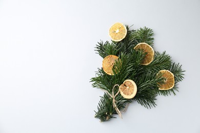 Photo of Christmas bouquet of fir tree branches with dry orange pieces on light background, top view. Space for text