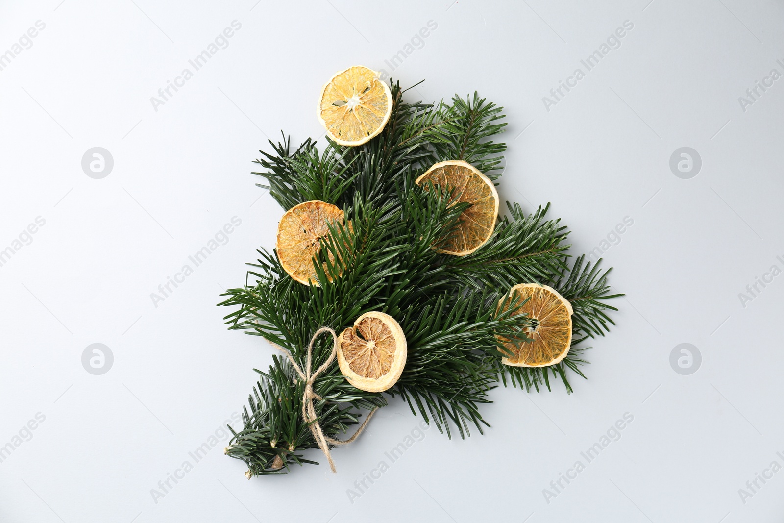 Photo of Christmas bouquet of fir tree branches with dry orange pieces on light background, top view