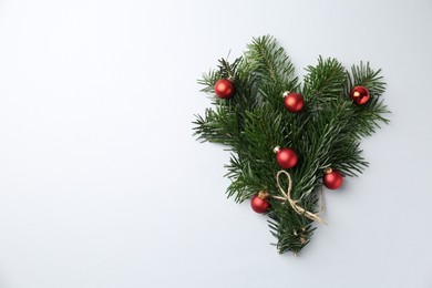 Photo of Festive bouquet of green fir branches with Christmas balls on light background, top view. Space for text