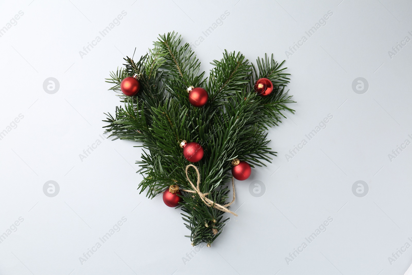 Photo of Festive bouquet of green fir branches with Christmas balls on light background, top view