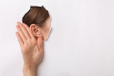 Photo of Woman showing hand to ear gesture through hole in white paper, closeup. Space for text