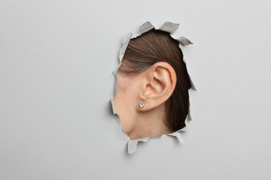 Photo of Woman showing her ear through hole in grey paper, closeup