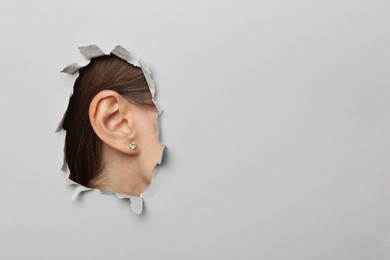 Photo of Woman showing her ear through hole in grey paper, closeup. Space for text