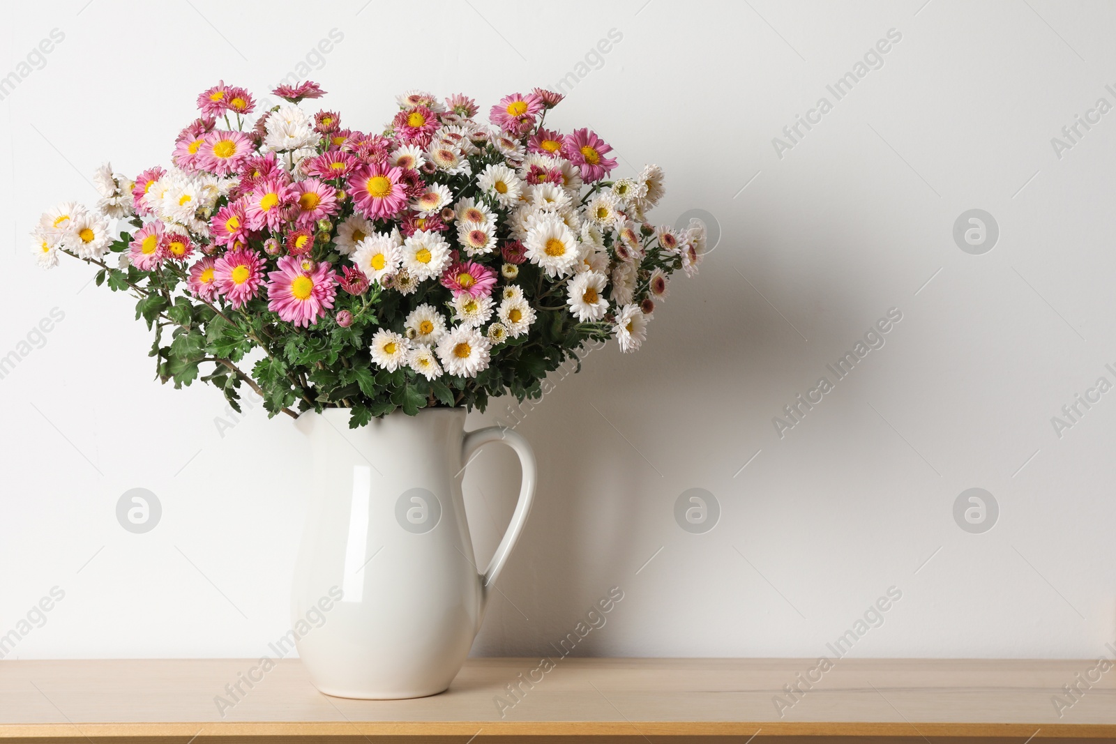 Photo of Vase with beautiful flowers on wooden shelf near white wall, space for text