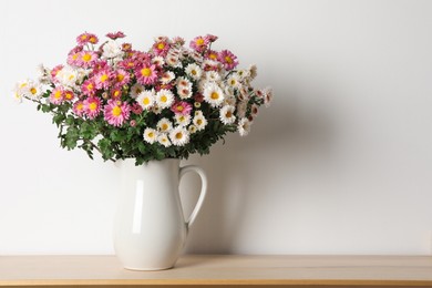 Photo of Vase with beautiful flowers on wooden shelf near white wall, space for text