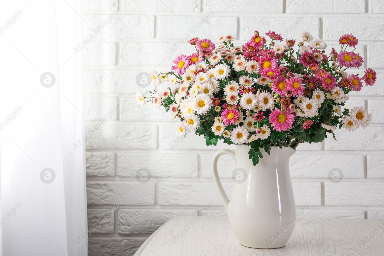 Photo of Vase with beautiful flowers on wooden table near white brick wall. Space for text