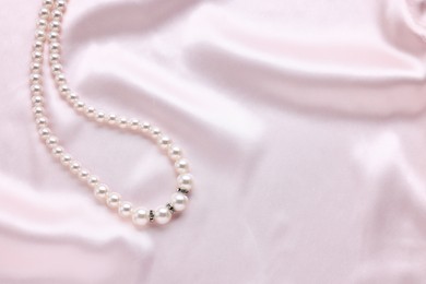 Photo of Elegant pearl necklace on pink fabric, top view. Space for text