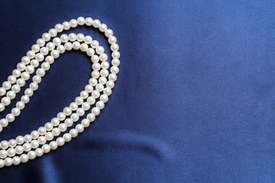 Photo of Elegant pearl necklace on dark blue fabric, top view. Space for text