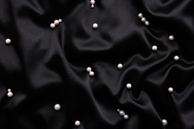 Photo of Many shiny pearls on black cloth, top view