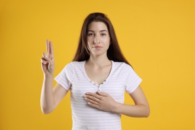 Woman showing oath gesture on orange background. Making promise