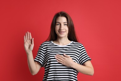 Woman showing oath gesture on red background. Making promise