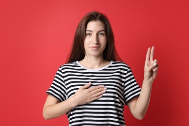 Woman showing oath gesture on red background. Making promise