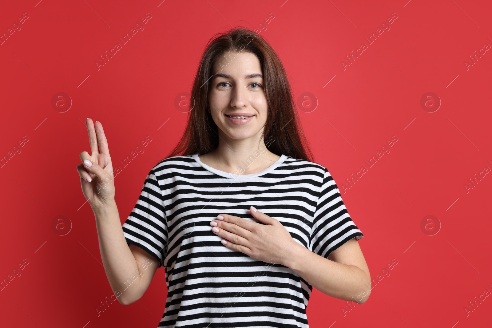 Photo of Woman showing oath gesture on red background. Making promise