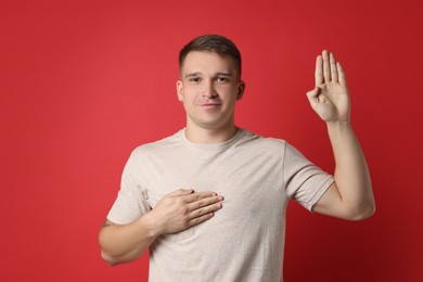 Photo of Man making promise with raised hand on red background. Oath gesture