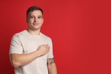 Photo of Man making promise on red background, space for text. Oath gesture