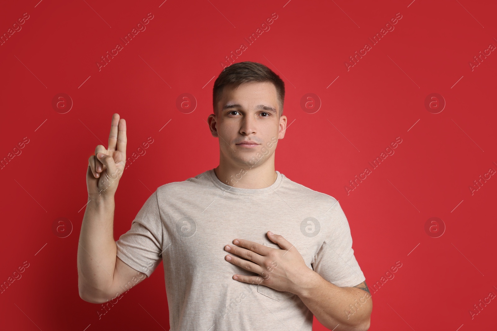 Photo of Man showing oath gesture on red background. Making promise